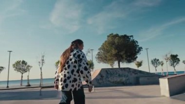 Genç bir kadın kaykay yapıyor, parkta kase oyuyor. Kız yazın kaykay parkında kaykaya biniyor. İzleme görüntüsü