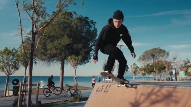 En skridskoåkare som övar på skateparken. Ung man gör skateboard tricks på skateboard park. — Stockvideo