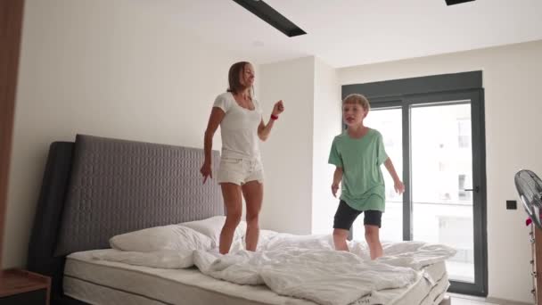 Mãe feliz se divertir pulando com o pequeno filho na cama . — Vídeo de Stock