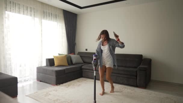 Zdjęcia młodej pięknej kobiety tańczącej i odkurzającej dywan w przytulnym pokoju w domu. Używa nowoczesnego odkurzacza. Jest szczęśliwa. — Wideo stockowe