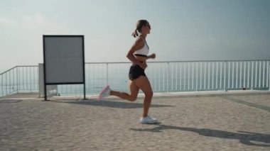 Genç beyaz kadın deniz kenarında koşuyor. Spor giyimli sıska kız deniz kenarında geziniyor..