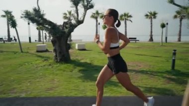 Sahilde koşan genç bir kadının açık hava fitness çekimi. Dişi koşucu deniz kenarındaki güvertede koşuyor..