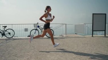 Genç beyaz kadın deniz kenarında koşuyor. Spor giyimli sıska kız deniz kenarında geziniyor..