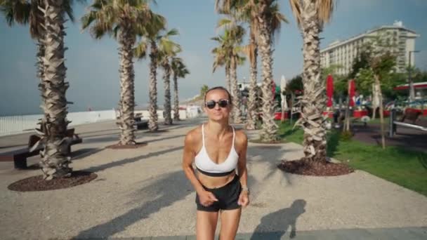 海辺を走っている若い白人女性 海によって遊歩道を走るスポーツウェアのスリム女の子 — ストック動画