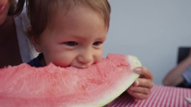 Genç anne ve kızı evde karpuz yiyorlar. Küçük oğlan, kırmızı karpuz yiyor..