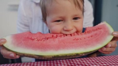 Genç anne ve kızı evde karpuz yiyorlar. Küçük oğlan, kırmızı karpuz yiyor..