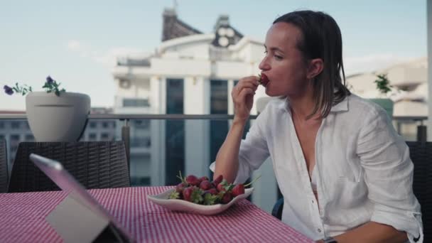 Koncentrerad Kvinna Äter Jordgubbar När Hon Använder Tabletten — Stockvideo