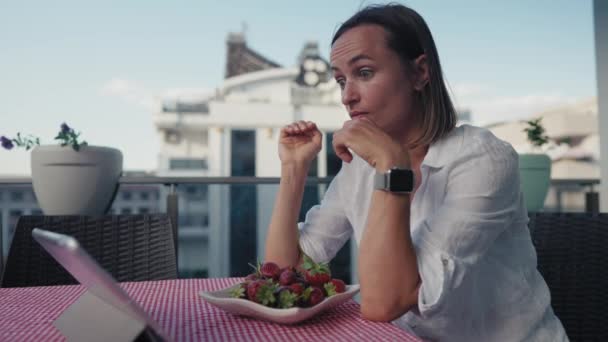 集中女性はタブレットを使用しながらイチゴを食べる — ストック動画
