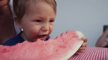 Genç anne ve kızı evde karpuz yiyorlar. Küçük oğlan, kırmızı karpuz yiyor..