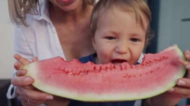 Genç anne ve kızı evde karpuz yiyorlar. Küçük oğlan, kırmızı karpuz yiyor..
