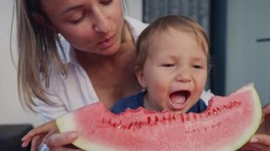 Genç anne ve kızı evde karpuz yiyorlar. Küçük oğlan, kırmızı karpuz yiyor..
