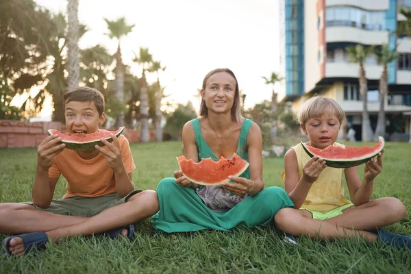 Sweet family, mother and her kids eating watermelon outdoor and having fun. High quality photo