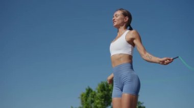 Genç bir kadın ip atlıyor. Genç bayan atlet ip atlıyor, açık havada sağlıklı olmak için antrenman yapıyor. Yavaş çekim