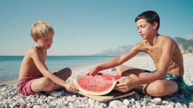 Mutlu çocuklar kumsalda büyük kırmızı dilim karpuz yeme.