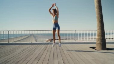 Sportswoman workout outdoor on seaside - she make burpee exercise. High quality 4k footage
