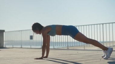 Şehirli bir sokakta güneşli bir sabahta genç kaslı bir kadın göğüs çalışıyor. Ağaçların yanındaki bankta şınav çeken çarpıcı kızın hareketini yakından izleyin. Sağlıklı yaşam tarzı kavramı. Yüksek kalite 4k görüntü