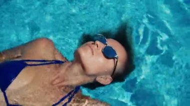 Genç bir bayanın yakın çekimi lüks bir oteldeki açık havuzda eğlenmek ve dinlenmektir. Yüksek kalite 4k görüntü