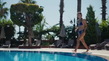 Mayo giymiş aktif genç bir kadın havuza dalıyor ve camlı su sıçrıyor. Yeşil palmiye ağaçları ve okyanusun arka planında dinlenirken havuza atlayan kız.. 