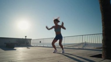 Sporcu kadın deniz kenarında spor yapıyor. Burpee egzersizi yapıyor. Yüksek kalite 4k görüntü