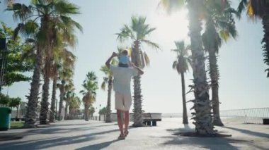 Father carrying son 12-17 months on shoulders and walking around at beach. Happy father and son playing on the beach at sunny day. High quality 4k footage