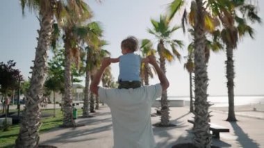 Father carrying son 12-17 months on shoulders and walking around at beach. Happy father and son playing on the beach at sunny day. High quality 4k footage