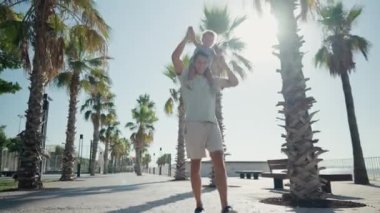 Father carrying son 12-17 months on shoulders and walking around at beach. Happy father and son playing on the beach at sunny day. High quality 4k footage