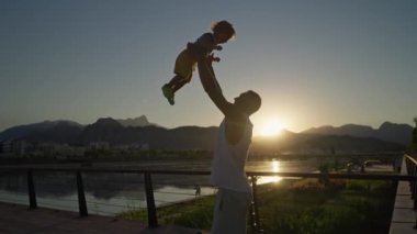 Mutlu bir aile. Baba oğlunu yukarı fırlatıyor. Baba gün batımında bebeğini atar. Mutlu aile kavramı. Babası oğlunu kollarına aldı ve günbatımında onu gökyüzüne fırlattı.
