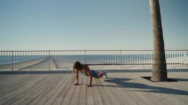 Sporcu kadın deniz kenarında spor yapıyor. Burpee egzersizi yapıyor. Yüksek kalite 4k görüntü