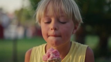 Outdoor portrait of young caucasian boy with blond hair eating ice cream in crispy cone.