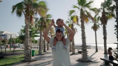 Father carrying son 12-17 months on shoulders and walking around at beach. Happy father and son playing on the beach at sunny day. High quality 4k footage