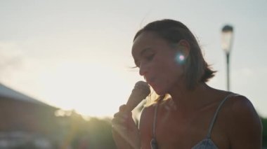 Beautiful blond girl eating ice cream in golden hour. Woman eating ice cream.