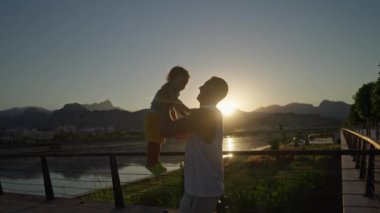 Mutlu bir aile. Baba oğlunu yukarı fırlatıyor. Baba gün batımında bebeğini atar. Mutlu aile kavramı. Babası oğlunu kollarına aldı ve günbatımında onu gökyüzüne fırlattı.