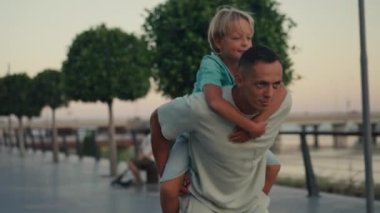 Piggyback family in park. Happy family in park. Father with son dream on green grass. Boy and dad are playing in park. Happy family concept. High quality 4k footage