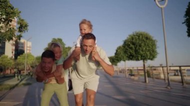 Father play with little children outdoor. Happy smiling father hold on back little son. Carefree weekend leisure and fun with kids outdoor concept. High quality 4k footage
