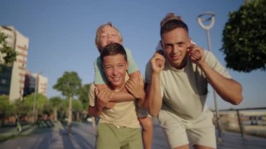 Father play with little children outdoor. Happy smiling father hold on back little son. Carefree weekend leisure and fun with kids outdoor concept. High quality 4k footage