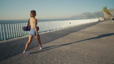 Yoga minderiyle köprüden yürüyen genç atletik bir kız. Yüksek kalite 4k görüntü