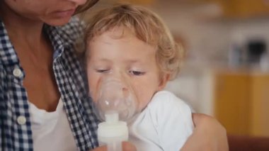 baby boy breathes through an inhaler or nebulizer while sitting in his mothers arms. High quality 4k footage