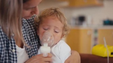 baby boy breathes through an inhaler or nebulizer while sitting in his mothers arms. High quality 4k footage