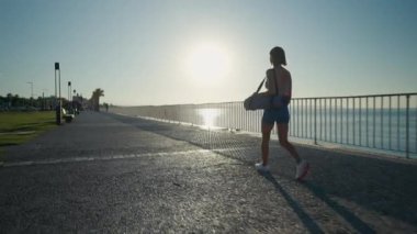 Sporty young athletic girl with a yoga mat walking over a bridge. High quality 4k footage