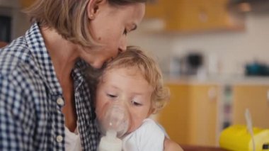 baby boy breathes through an inhaler or nebulizer while sitting in his mothers arms. High quality 4k footage