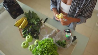 Young sportswoman putting washed greenery on table, and cooking smoothie. Happy vegetarian cooking healthy food and dancing. High quality 4k footage