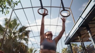 Healthy woman training gymnastics exercise using rings enjoying intense fitness workout. Caucasian sportswoman doing pull ups at street workout place. High quality 4k footage