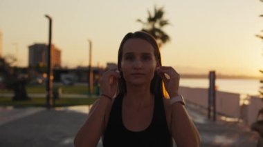 Portrait of attractive smiling happy brunette female runner running at seaside with airpods bluetooth headphones earphones. Healthy fitness athletic woman jogging outdoors. Motivation.