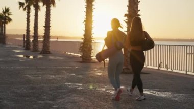 Sport and friendship. Outdoor portrait of two young caucasian women going home after fitness training, carrying fit mats, slow motion. High quality 4k footage
