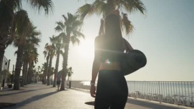 Fit woman with yoga mat and going to training. Caucasian woman walking on beach at the morning
