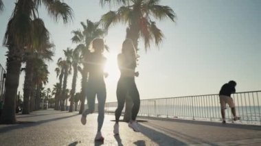 Two beautiful girls jogging at sunset or sunrise on beach. Young caucasian women running together. Brunette and blonde are smiling. Feeling of freedom while running. Concept of cardio.