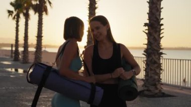 Sport and friendship. Outdoor portrait of two young caucasian women going home after fitness training, carrying fit mats, slow motion. High quality 4k footage
