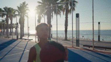 Young caucasian boy basketball player dribbling and practicing ball handling skill on court. Morning dusk, sun shines on the background. High quality 4k footage