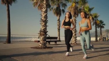 Two beautiful girls jogging at sunset or sunrise on beach. Young caucasian women running together. Brunette and blonde are smiling. Feeling of freedom while running. Concept of cardio.