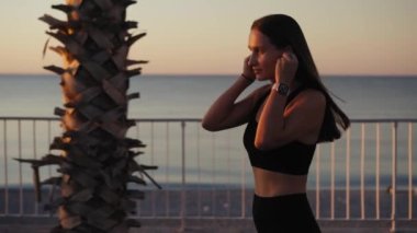 Portrait of attractive smiling happy brunette female runner running at seaside with airpods bluetooth headphones earphones. Healthy fitness athletic woman jogging outdoors. Motivation.